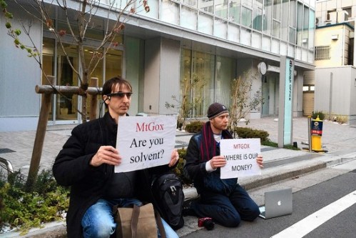 Bitcoin traders Kolin Burges, right, of London and Aaron, an American who gave only his first name, hold protest signs in front of the office tower housing Mt. Gox in Tokyo on Tuesday. (Associated Press)